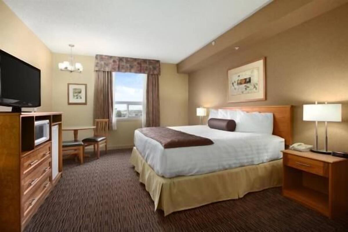 A hotel room with a bed, bedside lamps, a desk with a chair, a television, and a window with curtains.