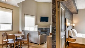 A hotel room with a dining area, a sofa, a TV mounted on the wall, and a fireplace. - Days Inn & Suites by Wyndham West Edmonton (Edmonton)