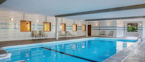 An indoor swimming pool with lounge chairs and a view of greenery outside.