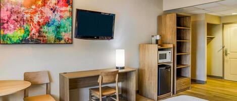 Une chambre d’hôtel équipée d’un bureau en bois, d’une chaise, d’un lit, d’une télévision, d’une bibliothèque et d’un four à micro-ondes.