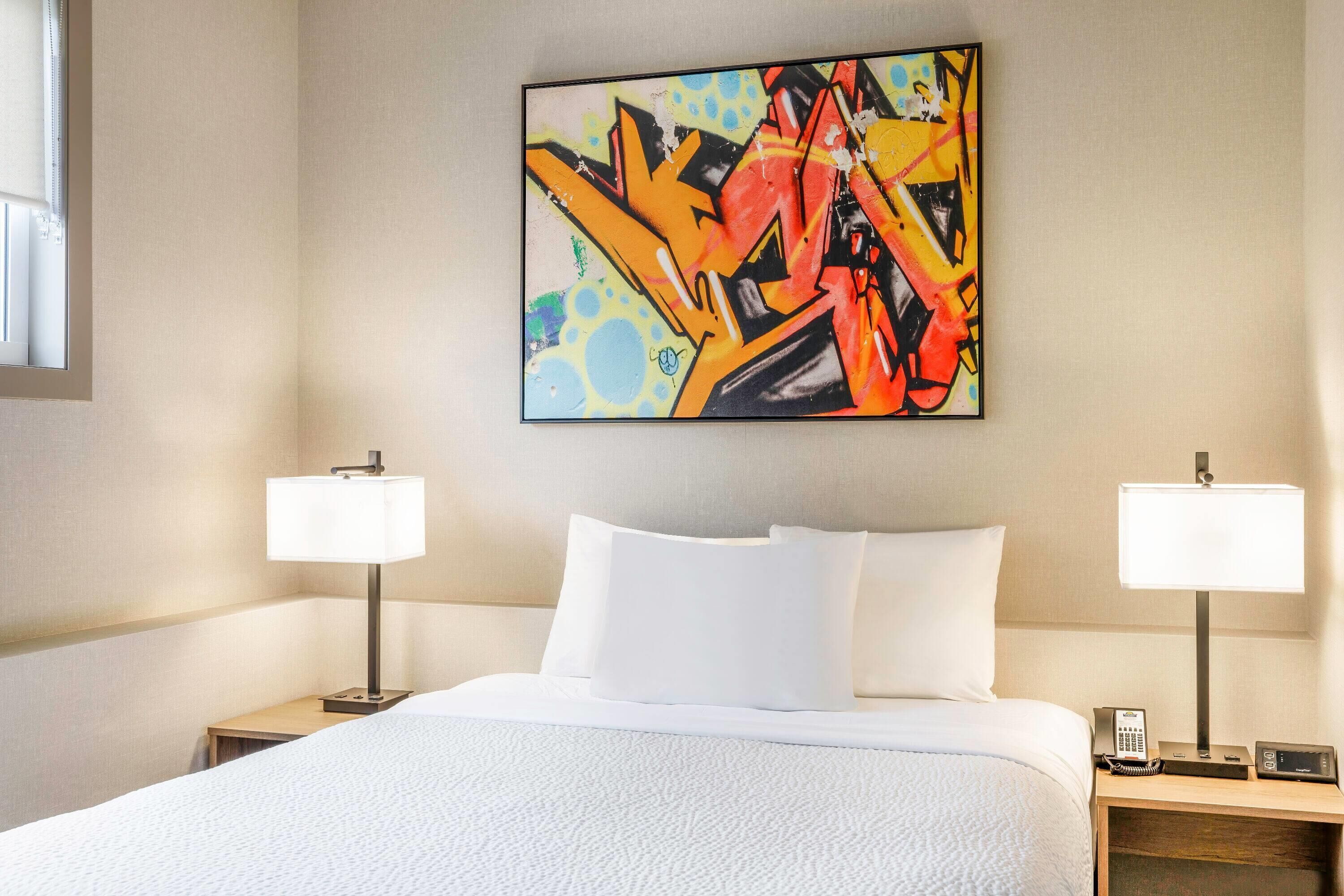 A hotel room with a large bed, two bedside tables with lamps, a wall-mounted artwork, and a window.