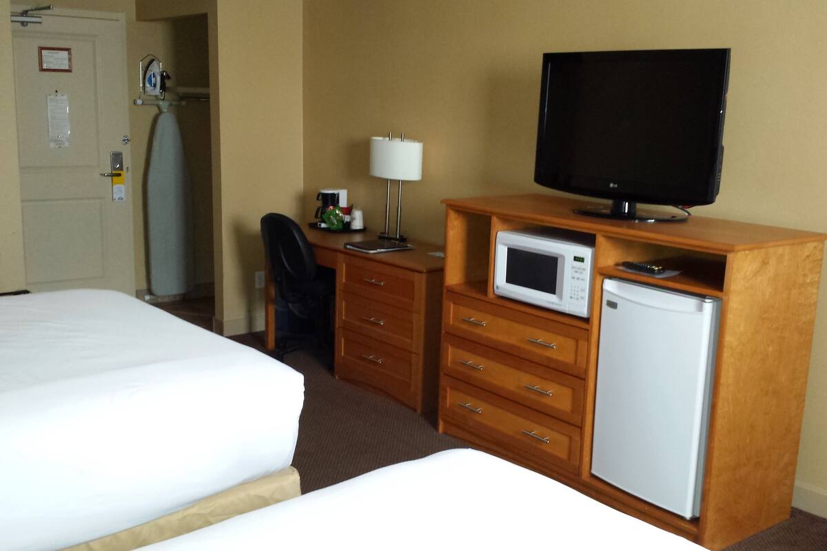 A hotel room with a bed, a desk with a television, a microwave, and a refrigerator.
