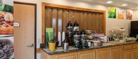 Un buffet de petit-déjeuner proposant une variété d’aliments et de boissons, notamment une machine à café, un mixeur et un présentoir de fruits.