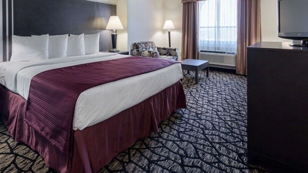 Quarto de hotel com uma cama grande, uma escrivaninha, uma televisão e uma janela com cortinas.