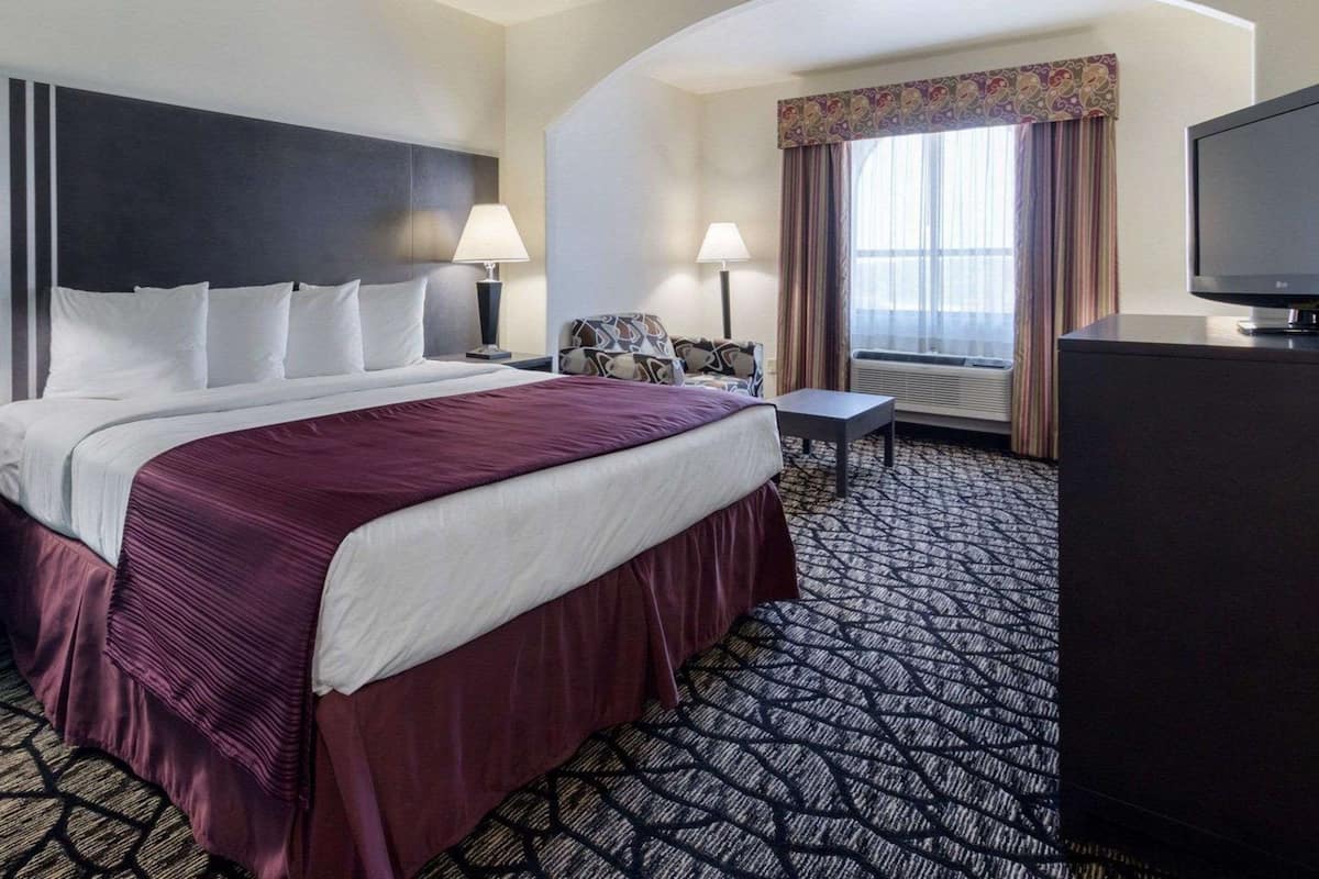 Une chambre d’hôtel avec un grand lit, un bureau, une télévision et une fenêtre avec des rideaux.