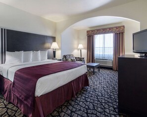 A hotel room with a large bed, a desk, a television, and a window with curtains.