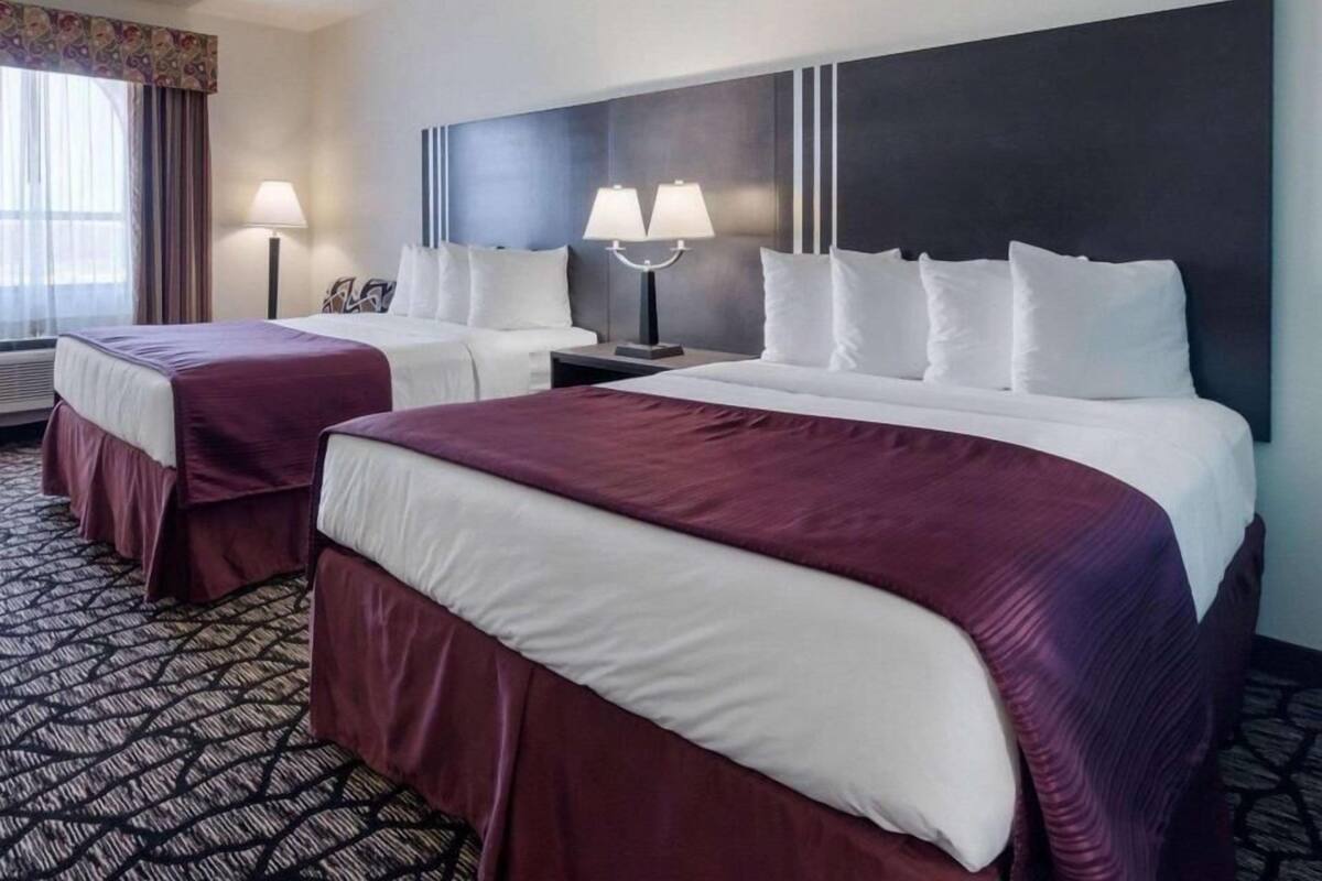 Une chambre d’hôtel avec deux lits, une grande tête de lit sombre, deux lampes de chevet et une moquette à motifs.