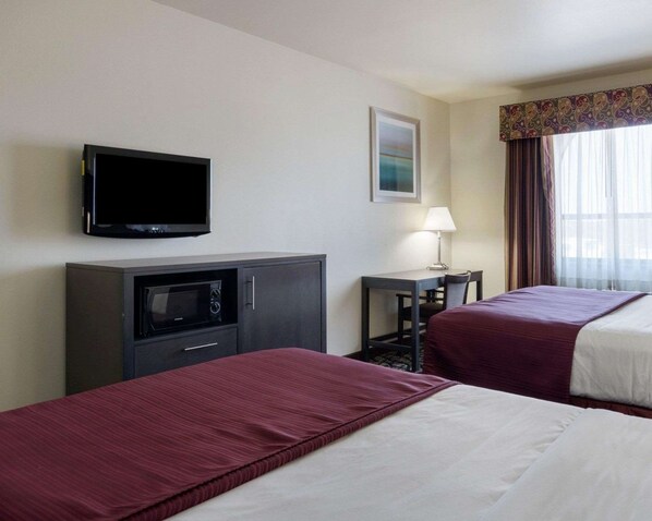 A hotel room with two beds, a TV, a desk with a lamp, and a window with curtains.