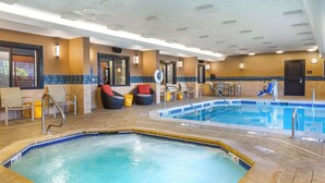 An indoor swimming pool with a hot tub, lounge chairs, and a tiled floor.