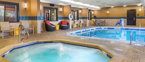 An indoor swimming pool with a hot tub, lounge chairs, and a tiled floor.