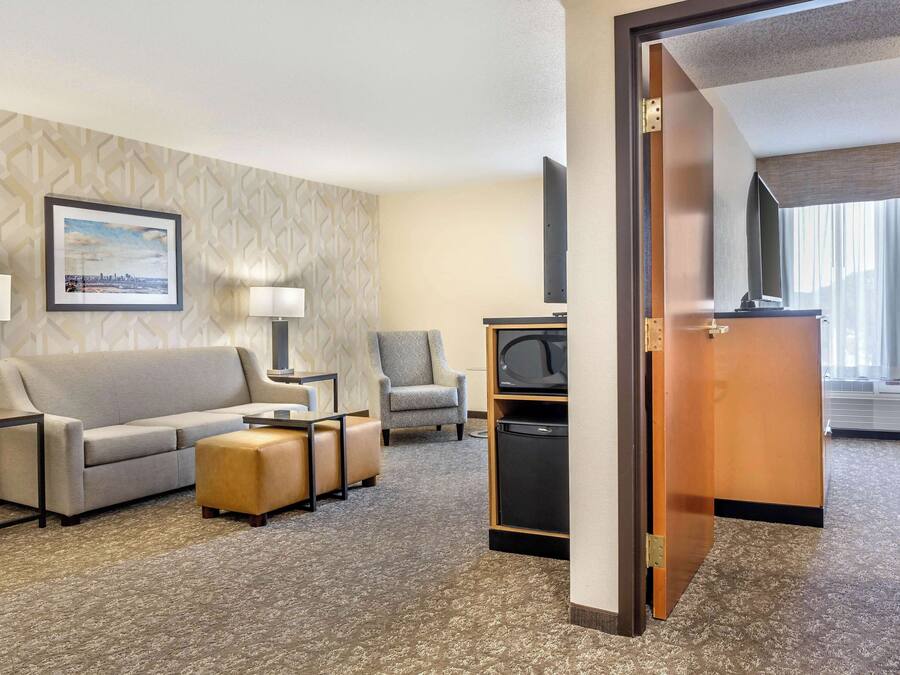 A hotel room with a sofa, ottoman, armchair, and a television on a stand.