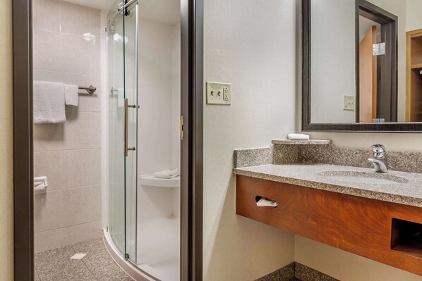 A modern bathroom with a glass shower enclosure, a granite countertop sink, and a wooden vanity. - Drury Inn & Suites Southwest St. Louis (Valley Park)