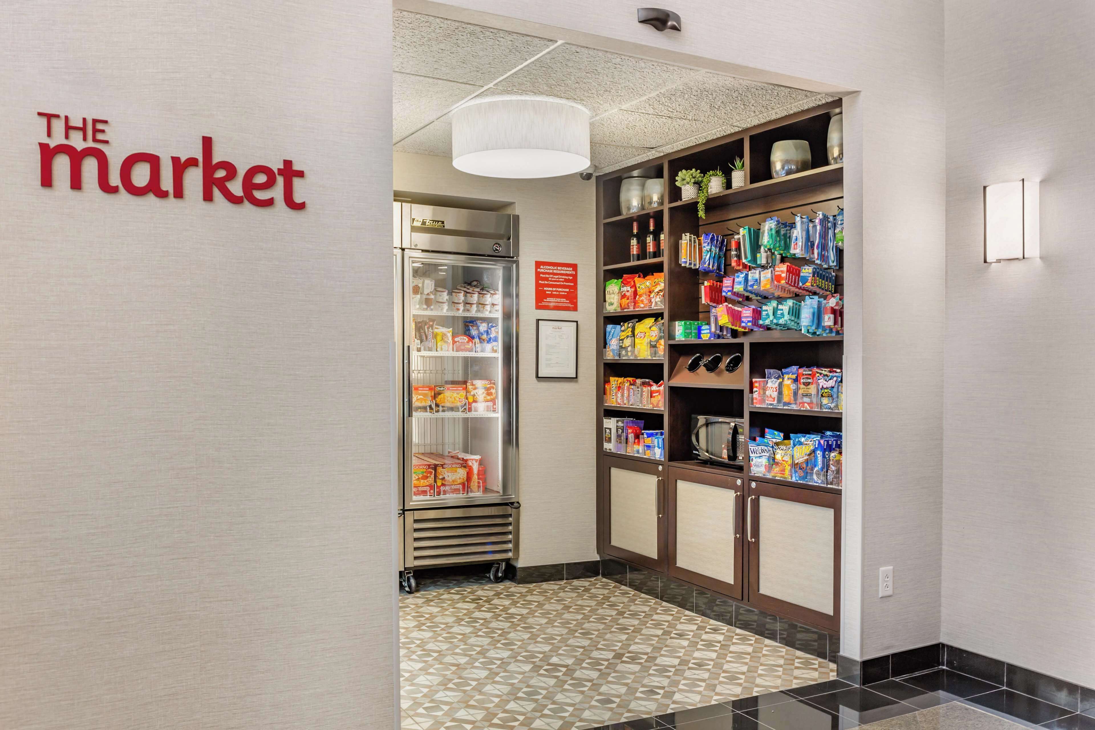 A hallway with a refrigerator stocked with food items, a pantry with various food products, and a sign reading "THE MARKET".