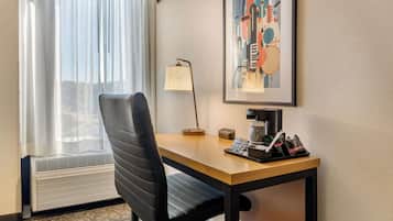 A hotel room with a desk, chair, lamp, and a framed abstract painting.
