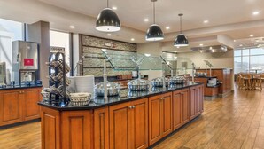 A modern hotel breakfast area with a central island, buffet setup, and a large window providing a view.