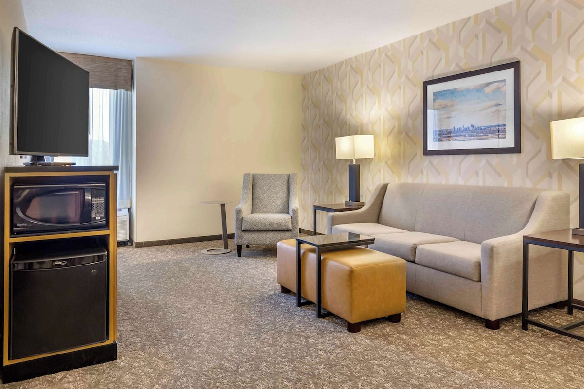 Ein Hotelzimmer mit Flachbildfernseher, Mikrowelle, Sofa, zwei Hocker, einem Sessel und einem Tisch mit Lampen.