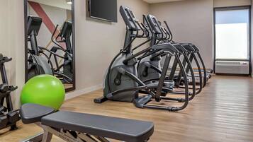 A gym with multiple exercise machines, a green exercise ball, and a bench.