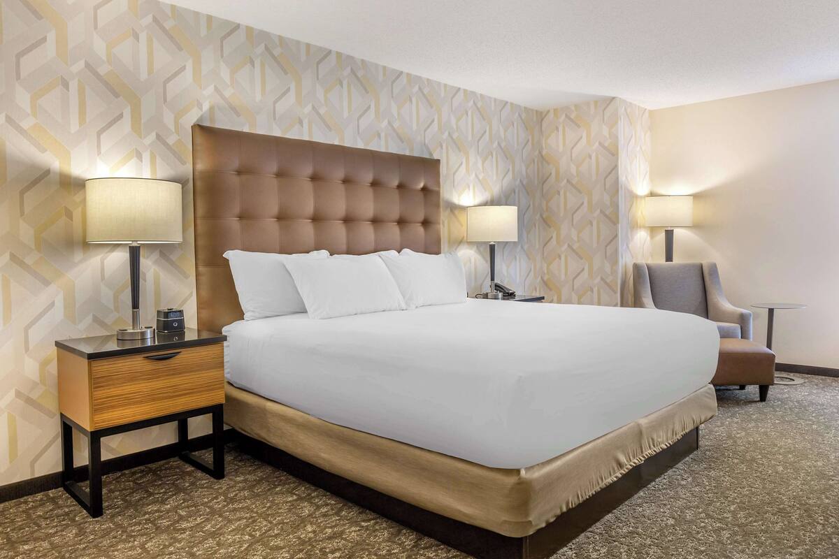 Ein Hotelzimmer mit einem großen Bett, zwei Nachttischen mit Lampen, einem Sessel und einer Wand mit Muster.