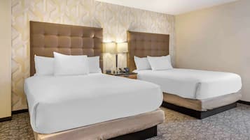 A hotel room with two beds, a patterned wall, a nightstand, and a lamp.