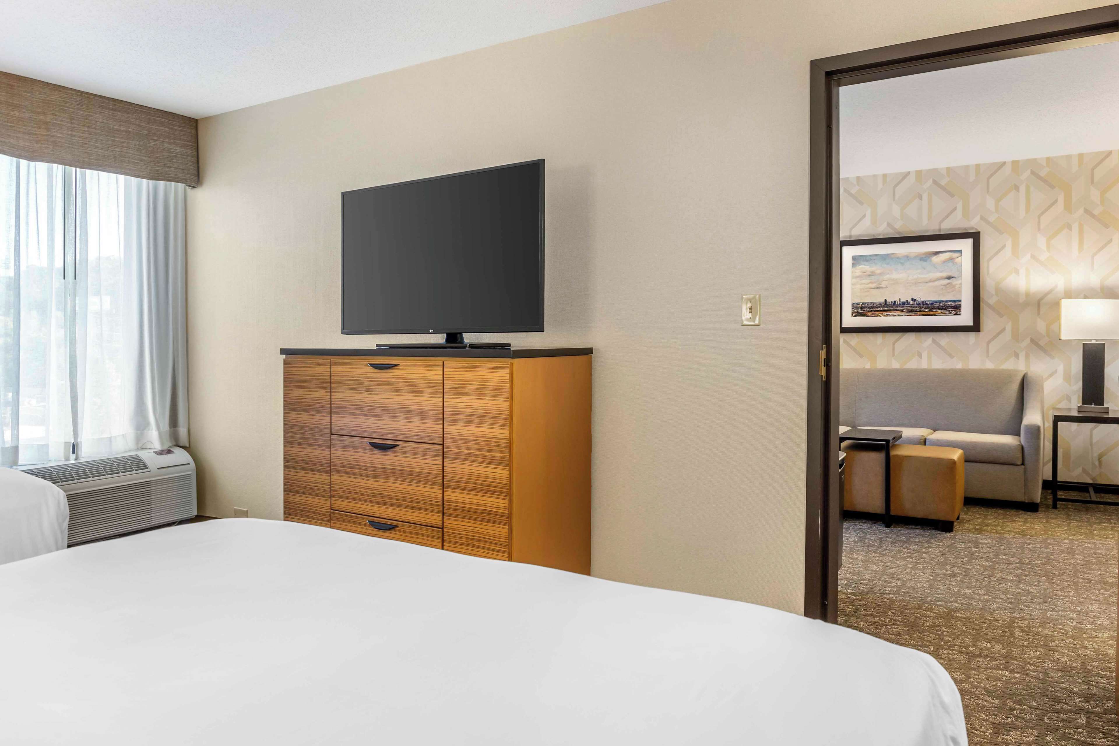 A hotel room with a bed, a TV on a wooden dresser, a sofa, and a lamp.