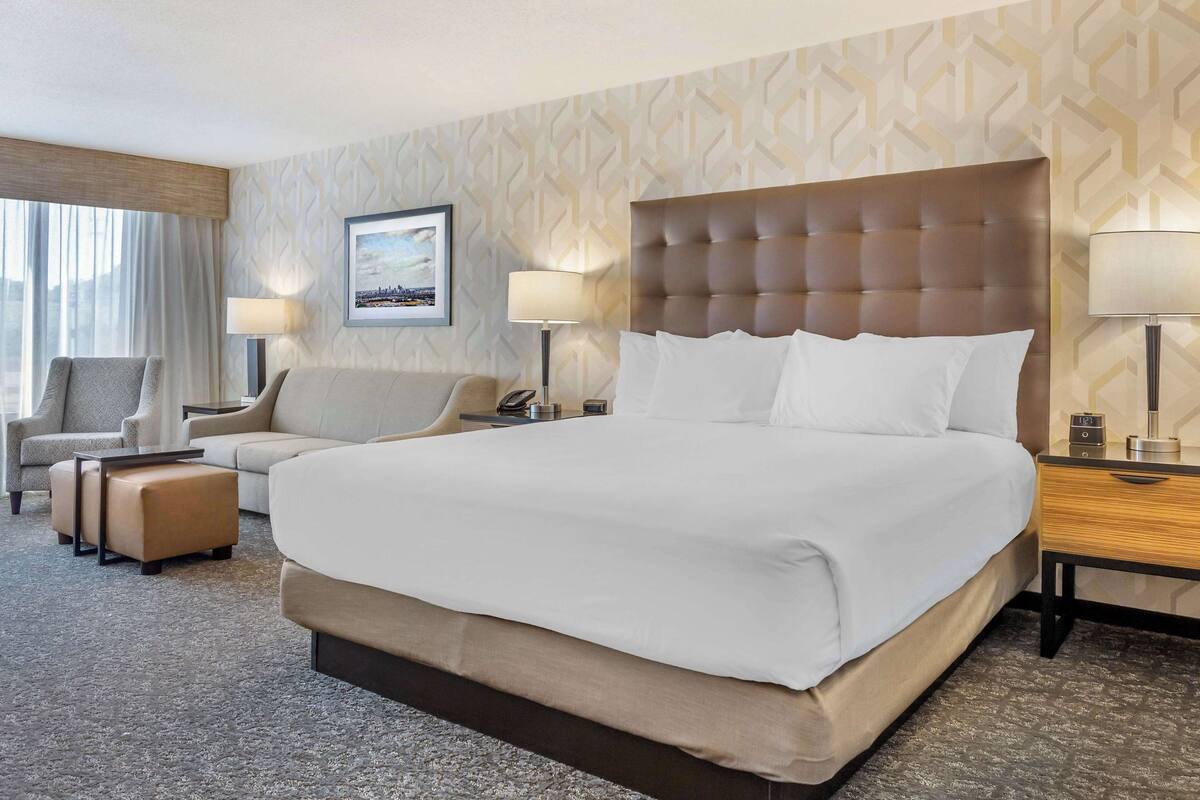 Ein Hotelzimmer mit einem großen Bett, einem Schlafsofa, einem Sessel und einem Schreibtisch mit Lampe.