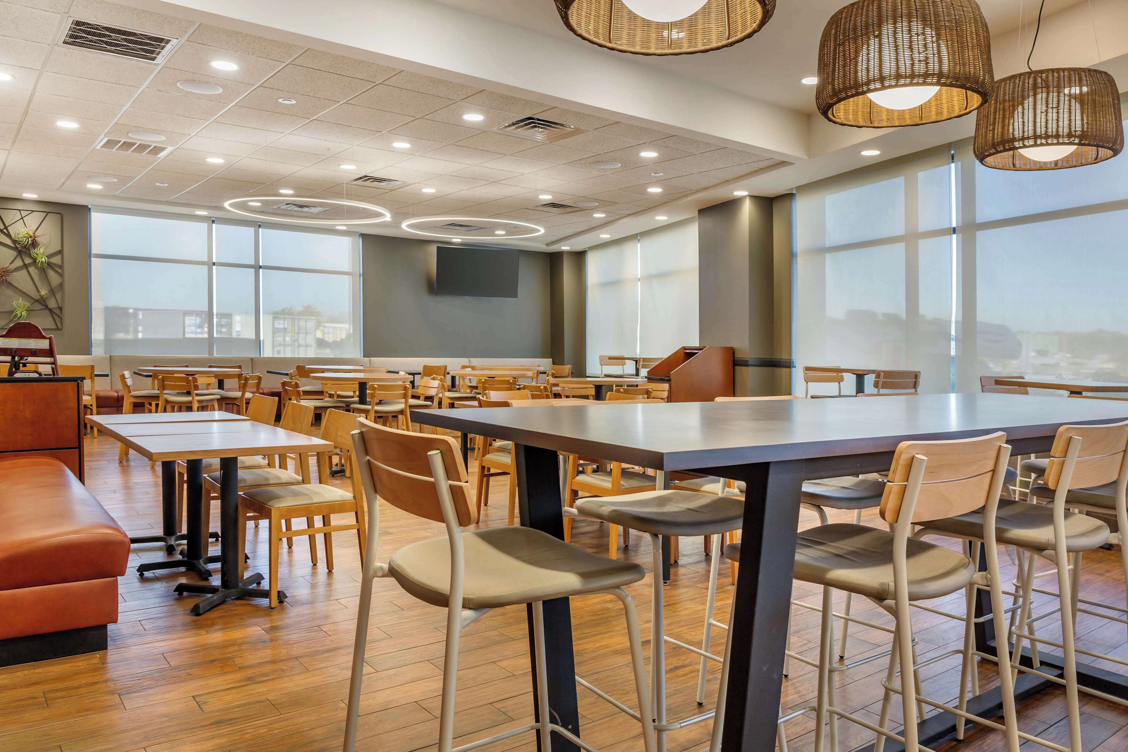 A spacious restaurant with high tables and chairs, large windows, and a modern ceiling design.
