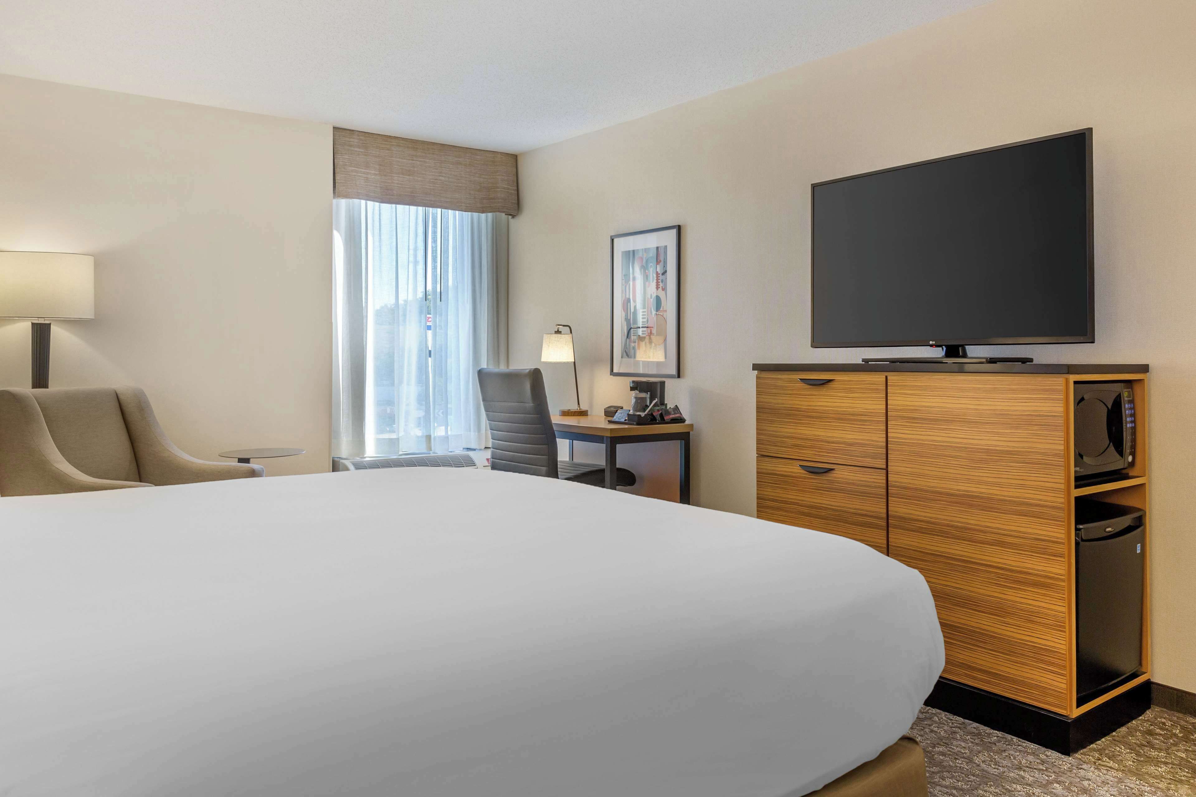 A hotel room with a large bed, a desk with a lamp, a television, and a wardrobe.