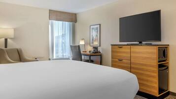 A hotel room with a large bed, a desk with a lamp, a television, and a wardrobe.