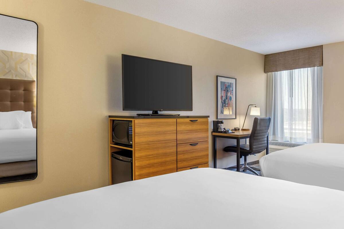 Ein Hotelzimmer mit einem großen Bett, einem Fernseher auf einer Holzkommode, einem Schreibtisch mit Stuhl und einem fenster mit Vorhängen.