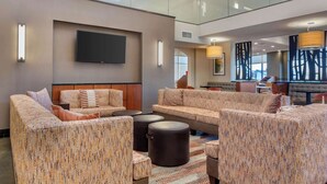 A spacious lobby with a high ceiling, a flat-screen TV mounted on the wall, and a seating area with sofas and ottomans.