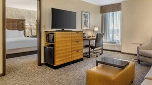A hotel room with a bed, a desk with a computer, a television, a sofa, and a window with a view.