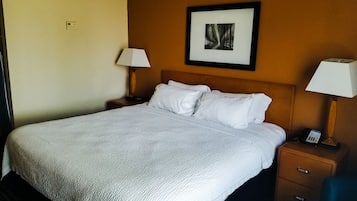 Een hotelkamer met een groot bed, twee nachtkastjes, een inlijsting foto aan de muur en een bijzettafeltje met telefoon.