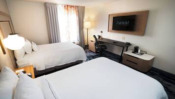 A hotel room with two beds, a desk, a TV, and a lamp.