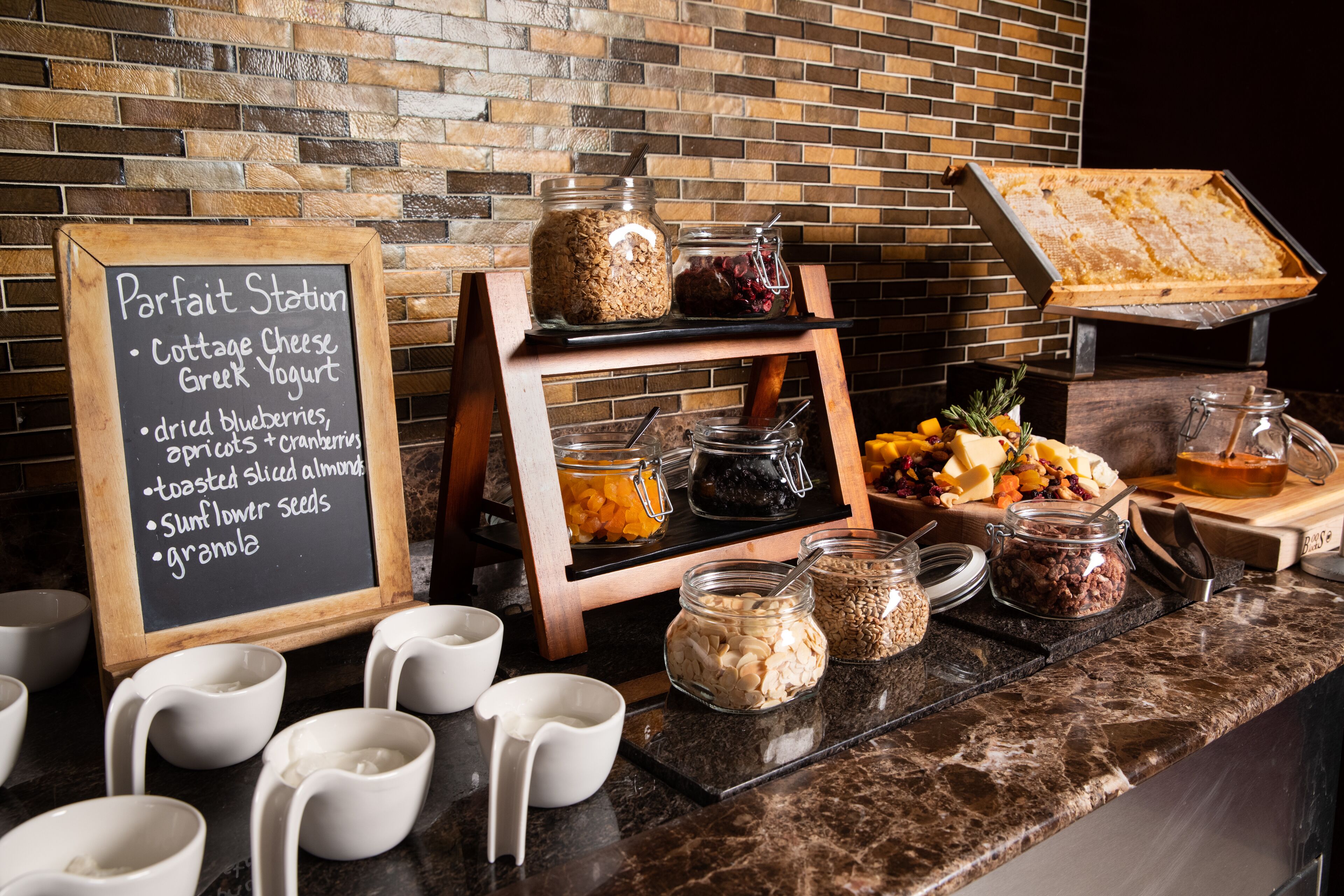 Un buffet de petit-déjeuner proposant une variété d’aliments, avec un panneau indiquant les différentes options, comme du fromage blanc, du yaourt grec et du granola.