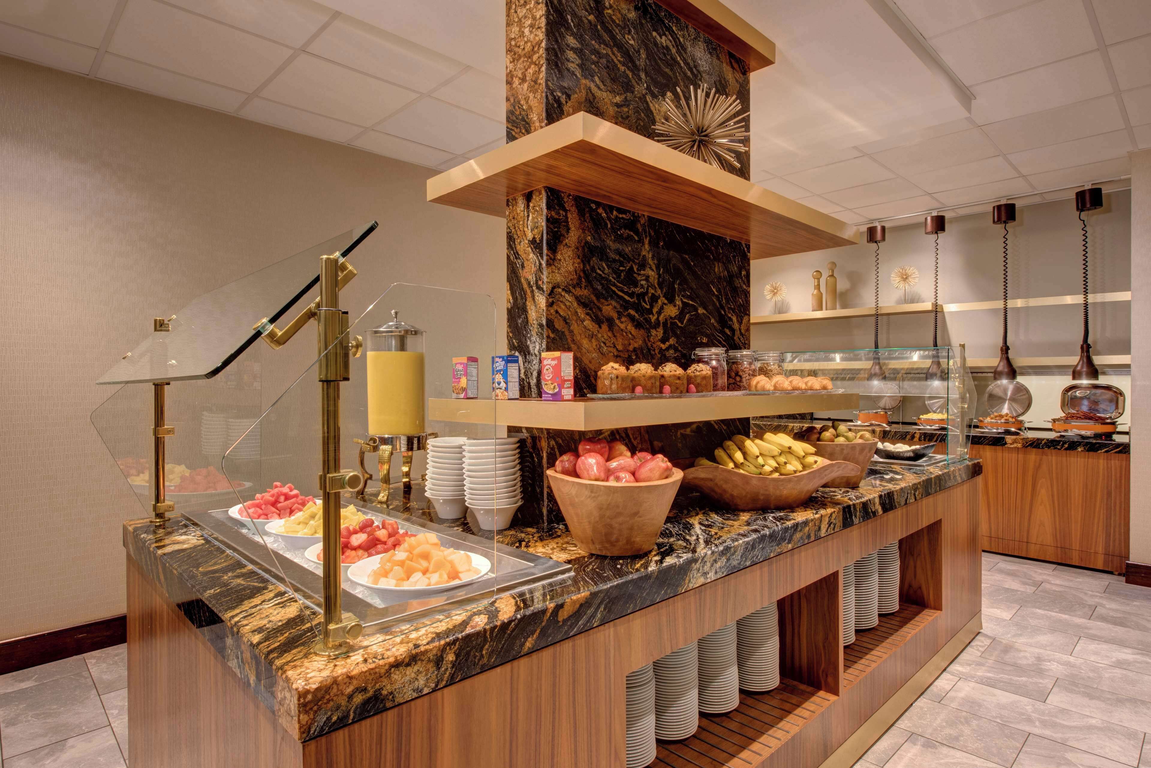 Un mostrador de buffet con diversos alimentos, una encimera de mármol y una estantería de madera con objetos decorativos.