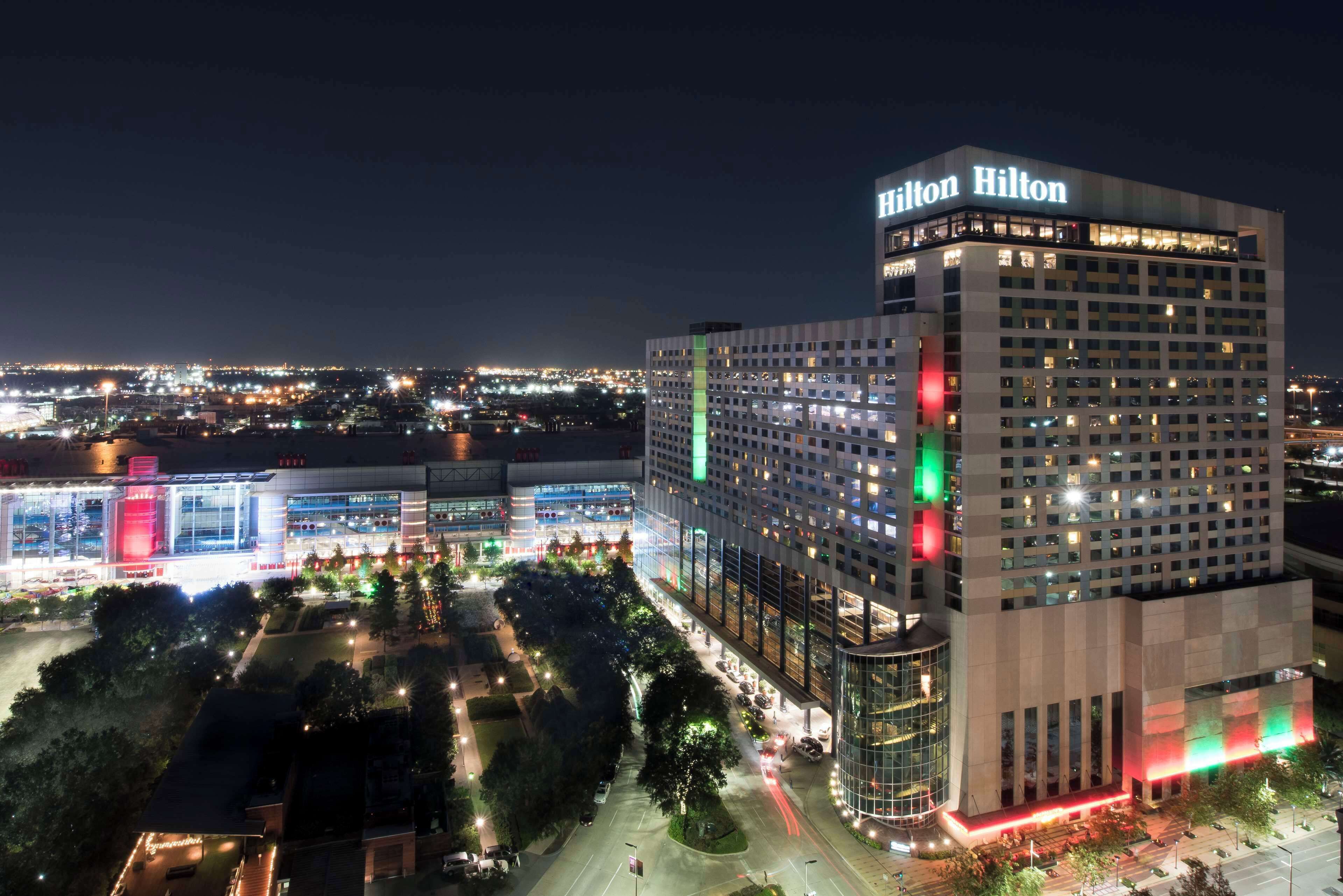 Un hotel de gran altura con un llamativo letrero de "Hilton", rodeado de calles bien iluminadas y otros edificios.