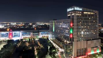 Un hotel de gran altura con un llamativo letrero de "Hilton", rodeado de calles bien iluminadas y otros edificios.
