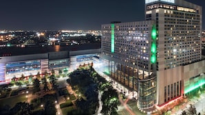 Um hotel moderno com uma placa Hilton em destaque, grandes janelas de vidro e uma área de recepção bem iluminada.