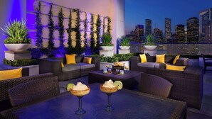 A rooftop lounge with outdoor seating, potted plants, and cocktails on a table. - Hilton Americas-Houston (Houston)