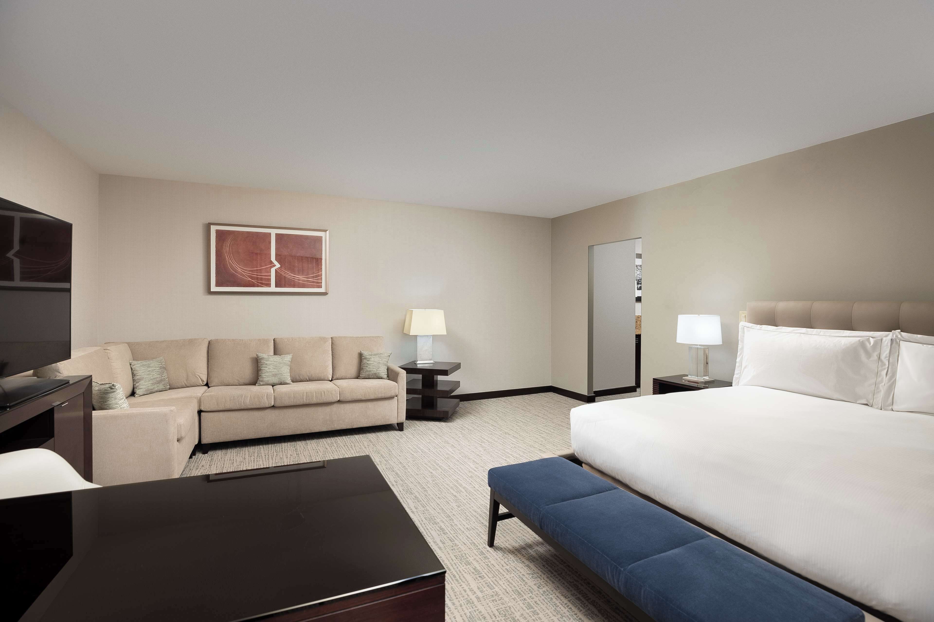 A hotel room with a bed, a sofa, a desk, and a TV.