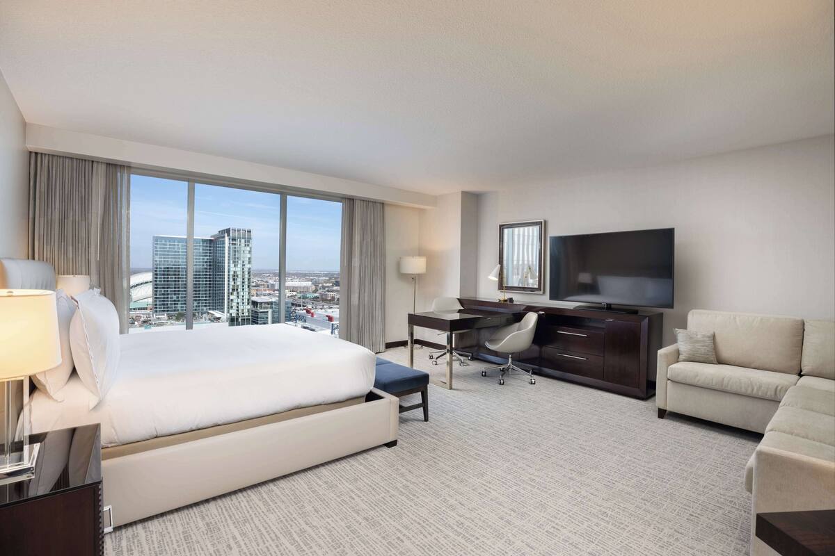 A hotel room with a large bed, a desk, a TV, and a view of the cityscape.