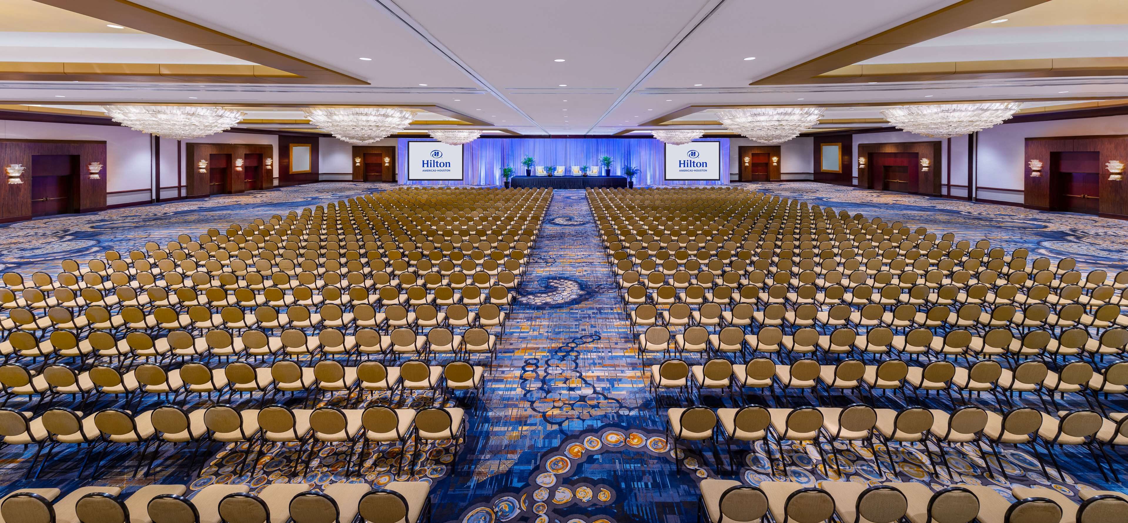 Une grande salle de conférence, avec des rangées de chaises disposées face à une scène ornée du logo de Hilton.