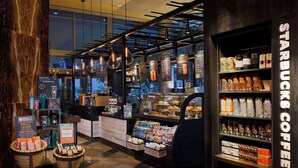 Interior de uma cafeteria Starbucks com design moderno, incluindo um balcão de café, prateleiras com produtos de café e uma exposição de sacas de café de origem única.
