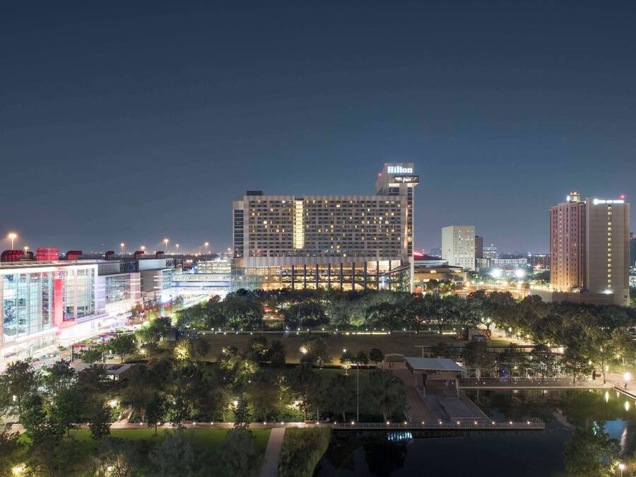 A modern hotel with a prominent Hilton sign, surrounded by lush greenery and a water feature.