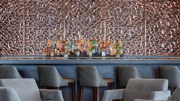 Zona de bar con pared de diseño geométrico, varias botellas de licor y taburetes.