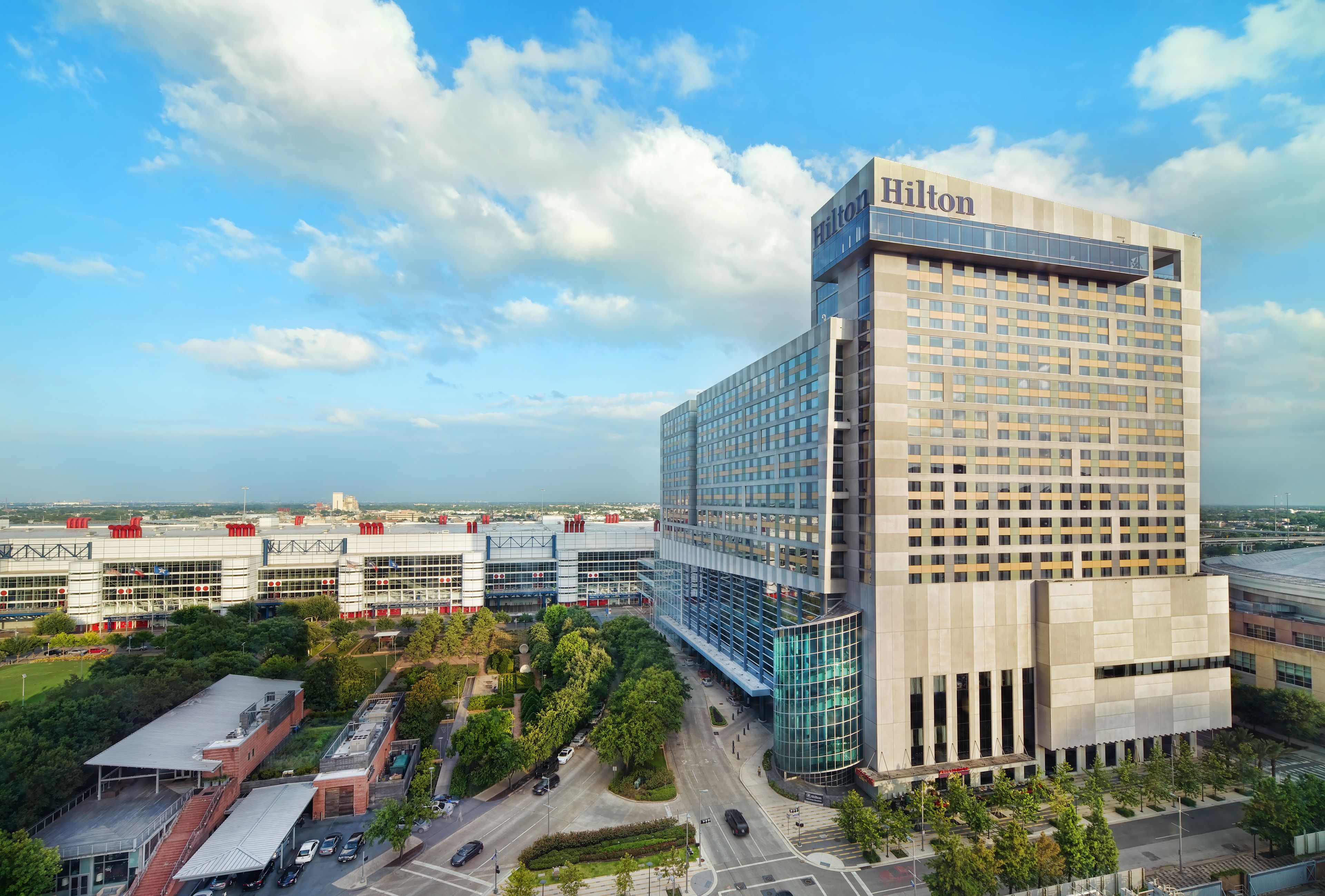 Un moderno hotel Hilton con una fachada de vidrio destacada, rodeado de vegetación y otros edificios.