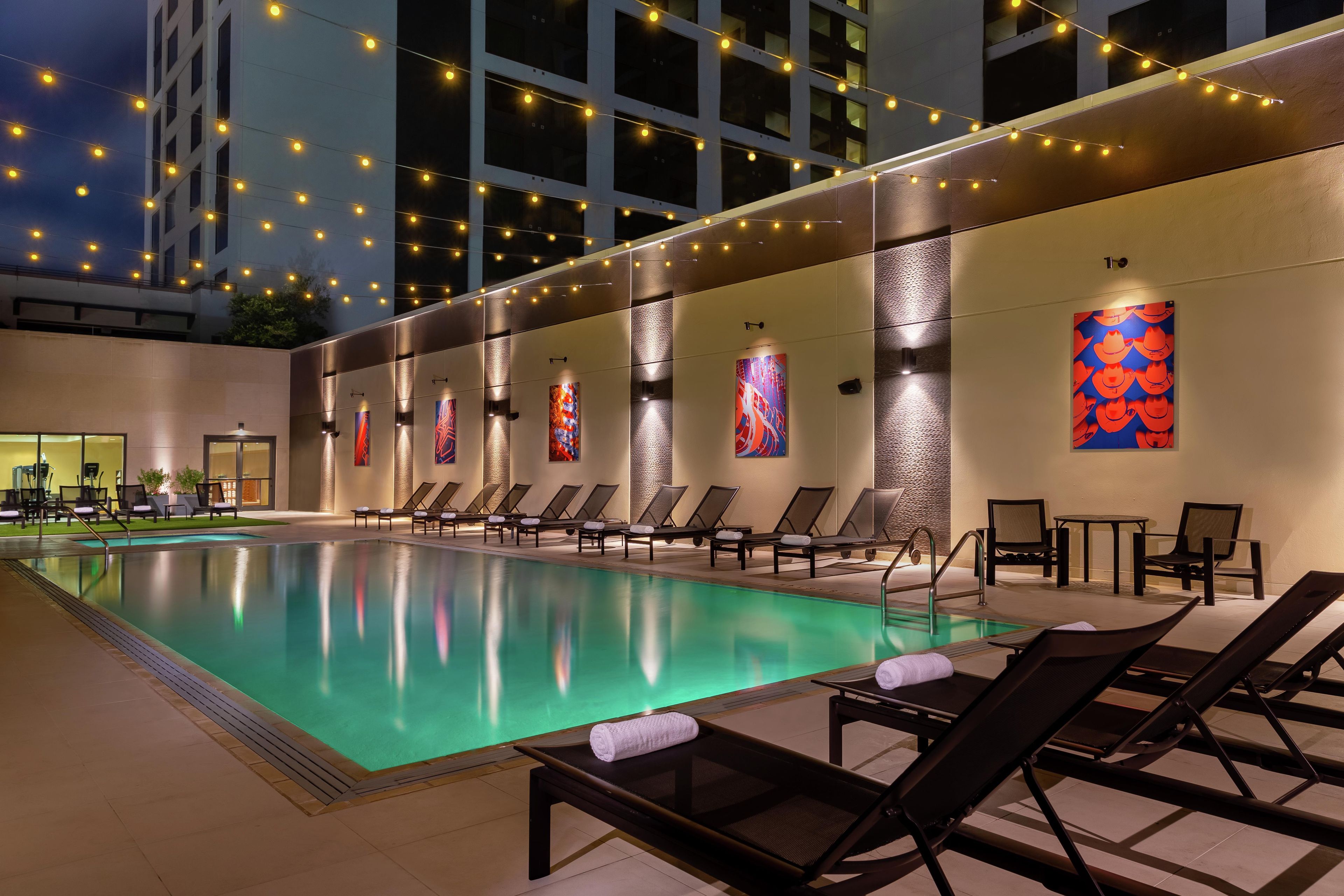 A pool area with lounge chairs, a tiled floor, and string lights.