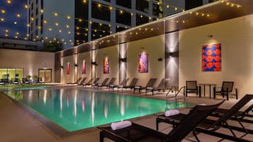 A pool area with lounge chairs, a tiled floor, and string lights.