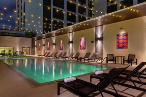 A pool area with lounge chairs, a tiled floor, and string lights. - Hilton Austin (Austin)