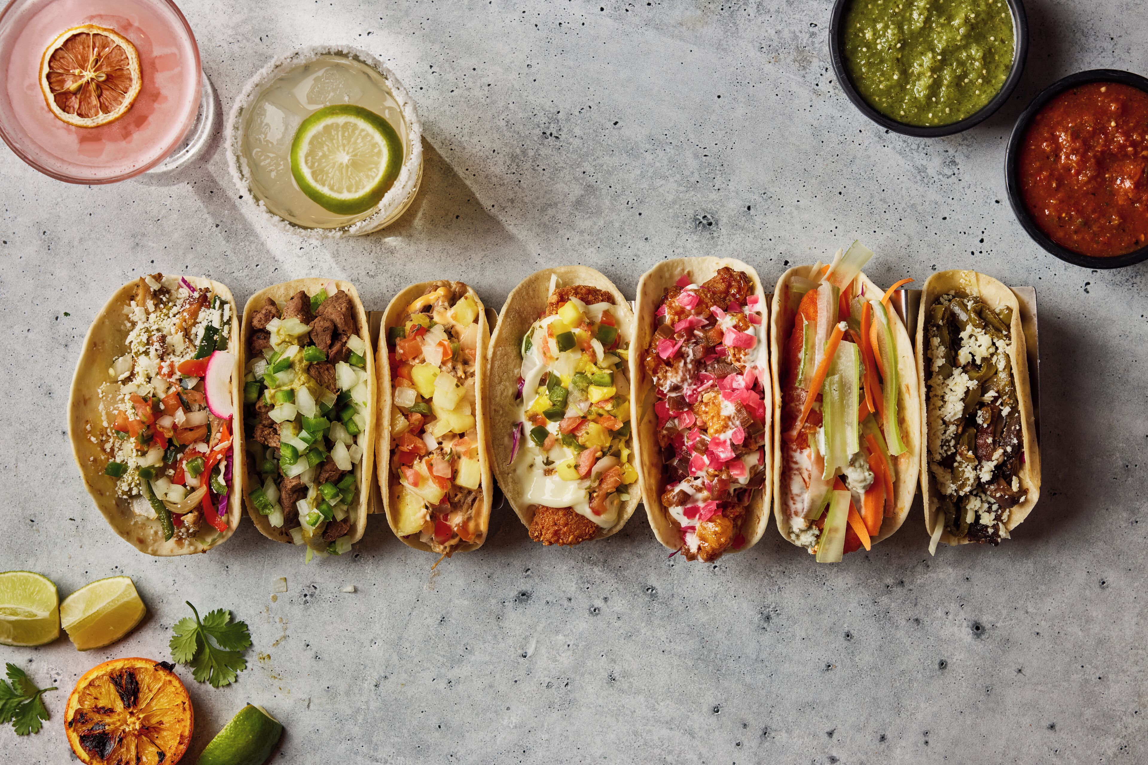 Variedad de tacos con diferentes ingredientes y tres porciones pequeñas de salsas.